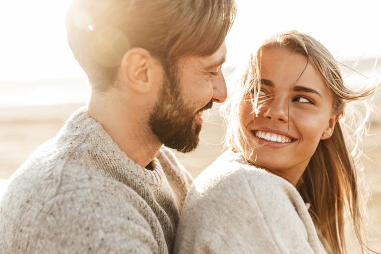 smiling beautiful young couple embracing while standing at the beach